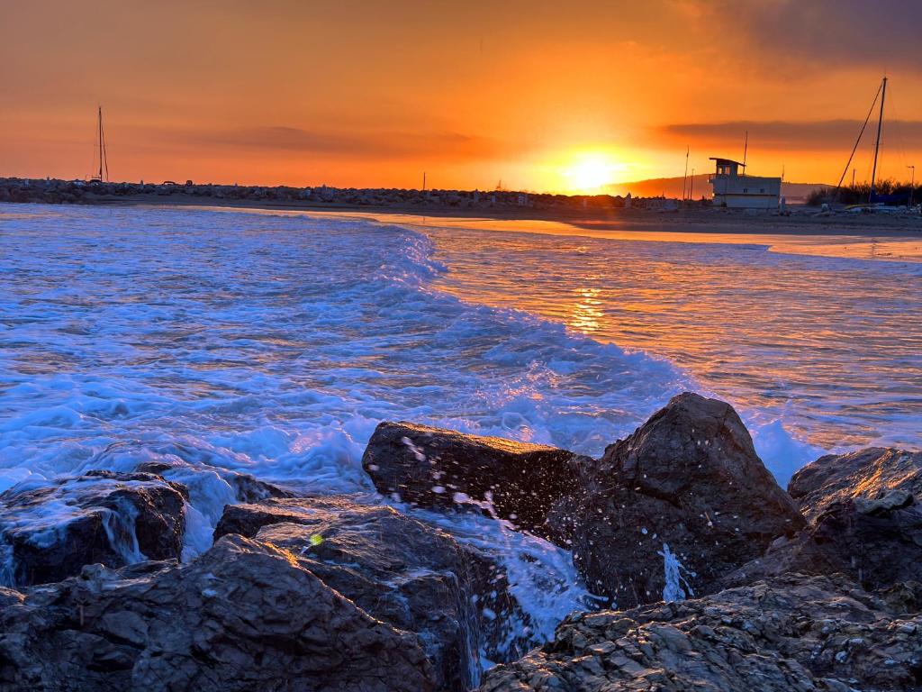 - un coucher de soleil sur la plage avec des rochers dans l'eau dans l'établissement Le chant des vagues, à Frontignan