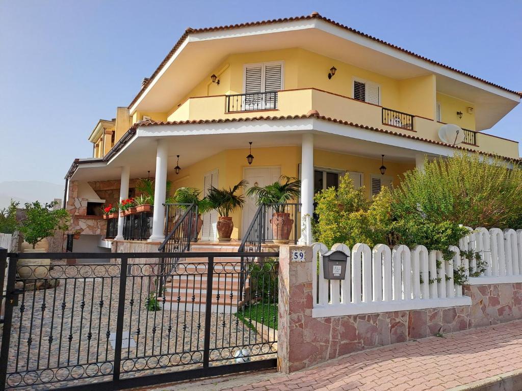 una casa amarilla con una valla blanca en ALICE B&B, en Villasimius