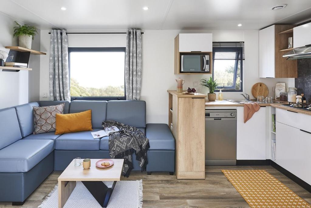 a living room with a blue couch and a kitchen at Camping de La Hallerais**** in Taden