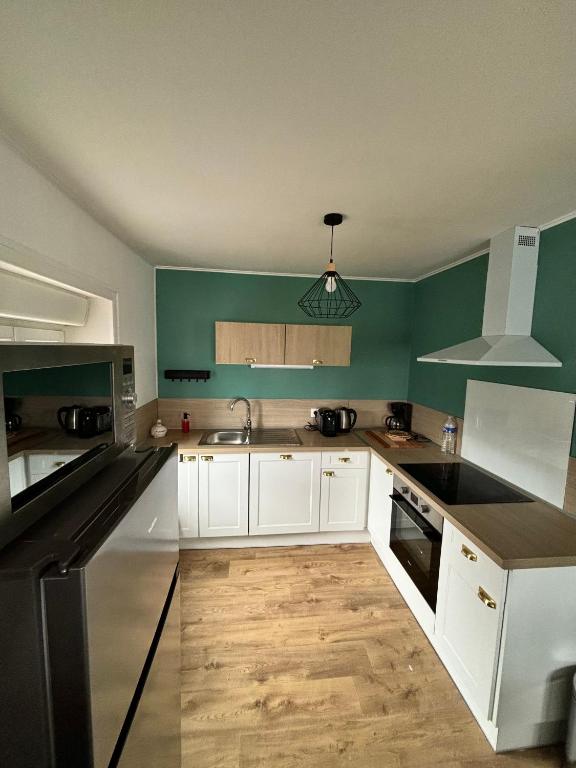 une cuisine avec des armoires blanches et des murs verts dans l'établissement LE QG, à Sainte-Mère-Église