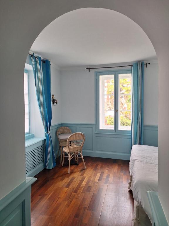 a bedroom with a bed and a table and two windows at Hotel Villa Catarie in Guéthary