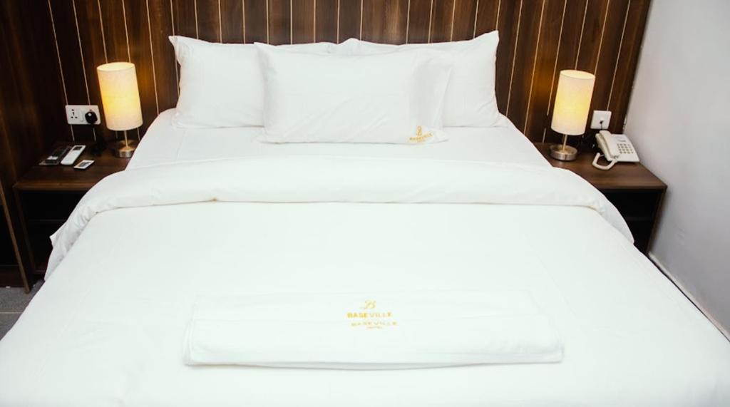Baseville Hotel في لاغوس: سرير بشرشف ابيض وجلستين ليليه بالمصابيح