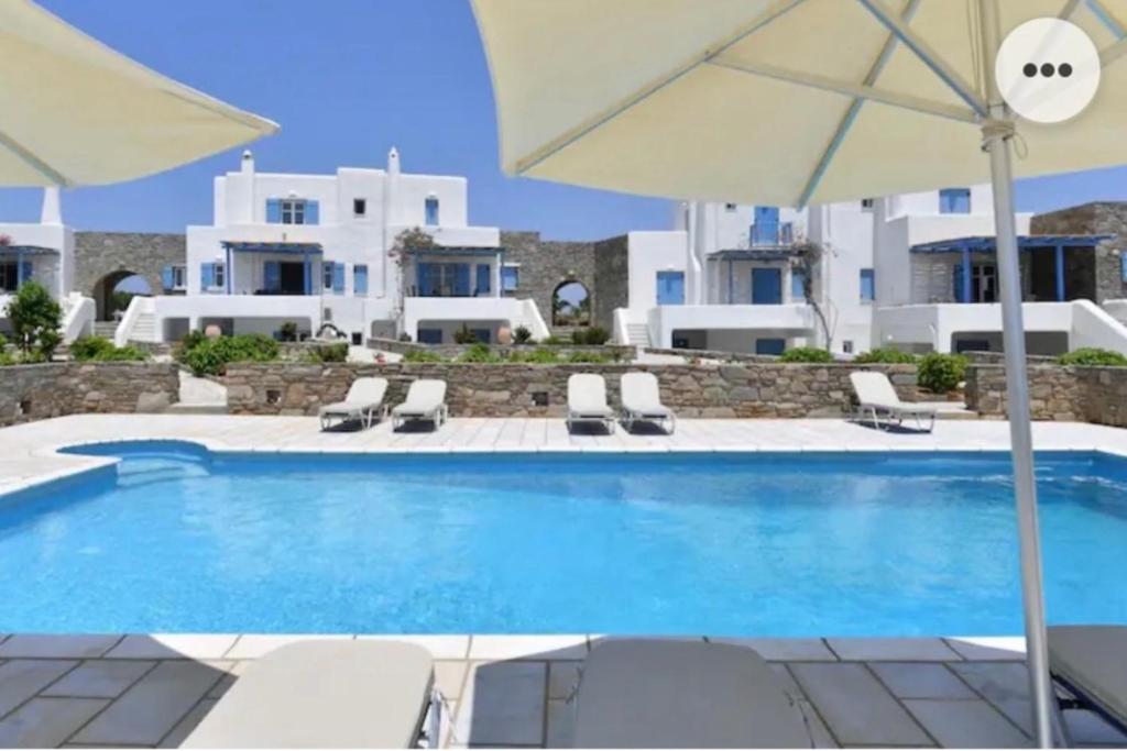 a pool with chairs and an umbrella and a building at Villa Galano PAROS GREECE in Ambelas