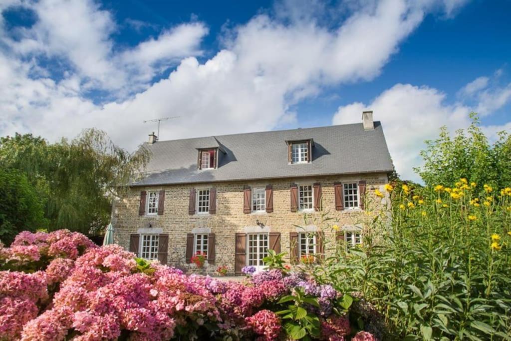 una gran casa de piedra con flores delante en Magnificent French Country House with Private Heated Pool & Gardens, en Quettreville-sur-Sienne
