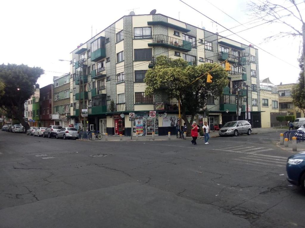 a city street with a large building with cars parked at Sunny Apartment Narvarte in Mexico City