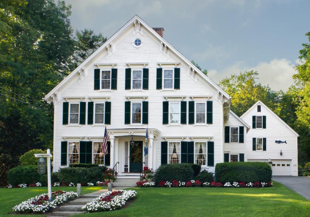 a white house with a flag and flowers at Camden Maine Stay Inn in Camden