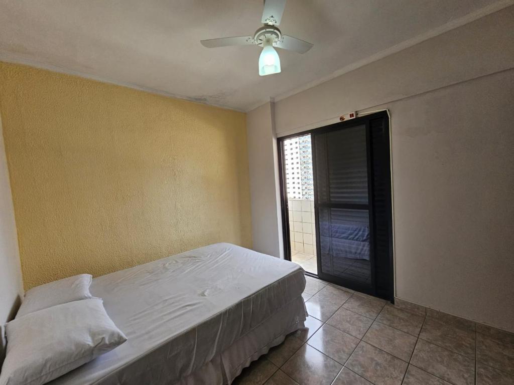 een slaapkamer met een bed en een plafondventilator bij Tupi Vista MAR III com VARANDA - 3 dormitórios - 50 metros da praia - com área de lazer PISCINA e salão de jogos - ESTACIONAMENTO gratuito in Praia Grande