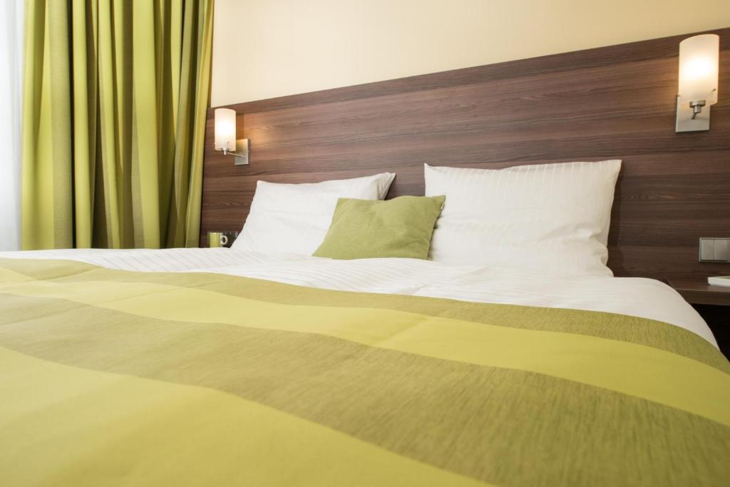 uma cama grande com lençóis brancos e almofadas verdes em Goethe Conference Hotel by Trip Inn em Frankfurt am Main