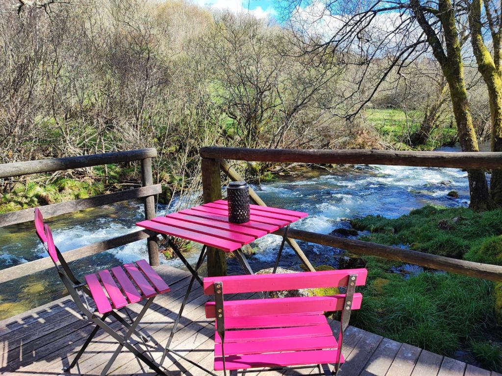 a pink table and two chairs on a deck next to a river at Moinhos do Poço Verde - Nova Gestão in Castro Laboreiro