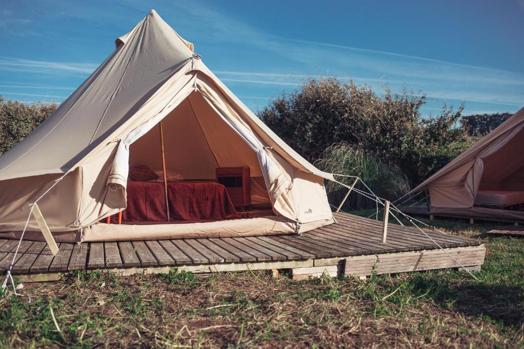 The Glamping Spot - Douarnenez في Plonévez-Porzay: خيمة قماش وسطح خشبي في حقل