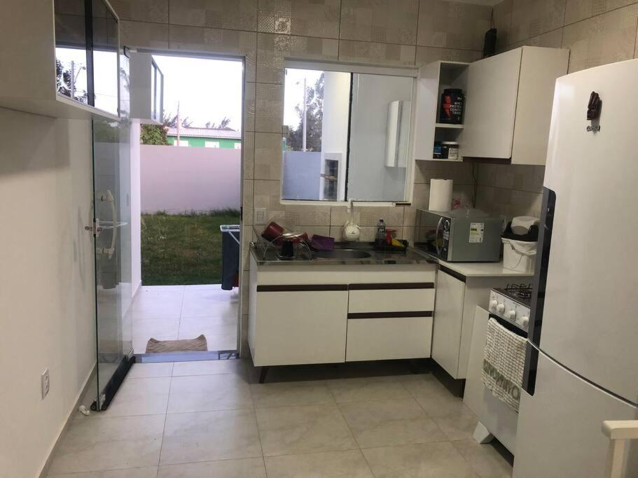 une cuisine avec des placards blancs et une grande fenêtre dans l'établissement Casa em Atlântida Sul, com 2 quartos e 2 banheiros, com ar condicionado., à Xangri-lá
