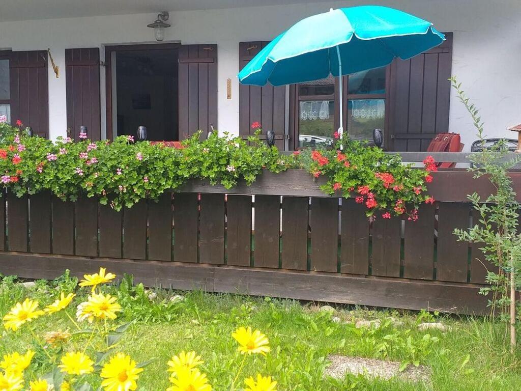 a wooden fence with a blue umbrella and flowers at Reindler Modern retreat in Fischen