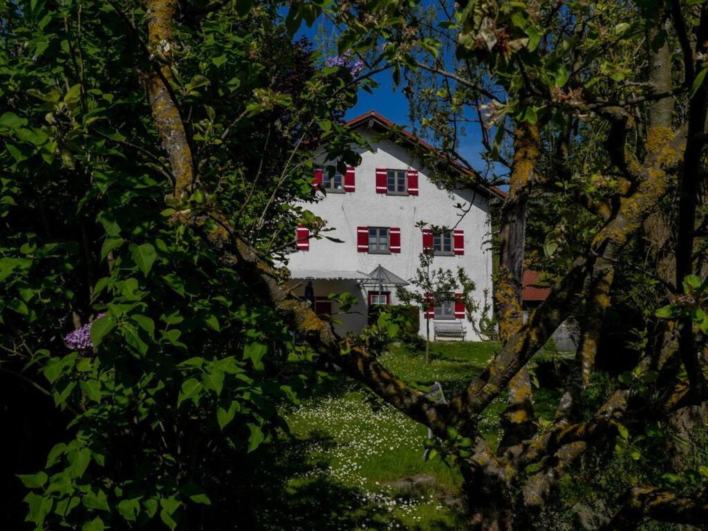 a white house with red windows through the trees at Hauser-Hof Modern retreat in Marktoberdorf