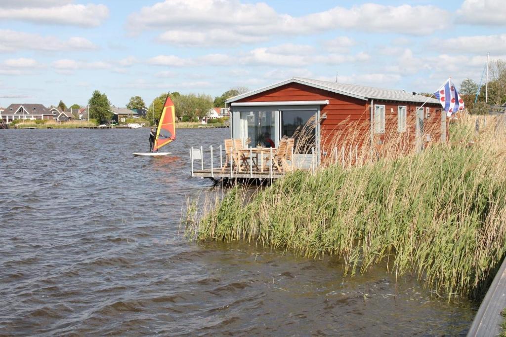 ein kleines Haus auf dem Wasser mit einem Segelboot in der Unterkunft Hausboot Schiff für 4 Personen ca 85 m in Oudega, Friesland Küste von Friesland in Oudega