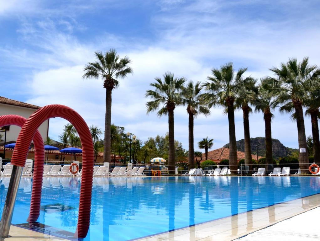 uma grande piscina com palmeiras e cadeiras em Villaggio Turistico La Mantinera - Residence em Praia a Mare