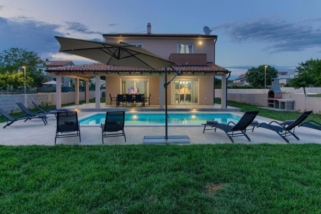 una piscina con sillas y una sombrilla frente a una casa en Ferienhaus mit Privatpool für 8 Personen ca 178 qm in Pula, Istrien Istrische Riviera, en Pula