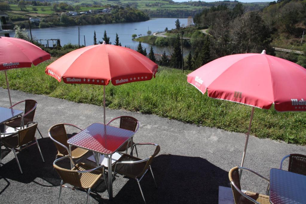 a table and chairs with red umbrellas and a lake at Albergue Ferramenteiro in Portomarin