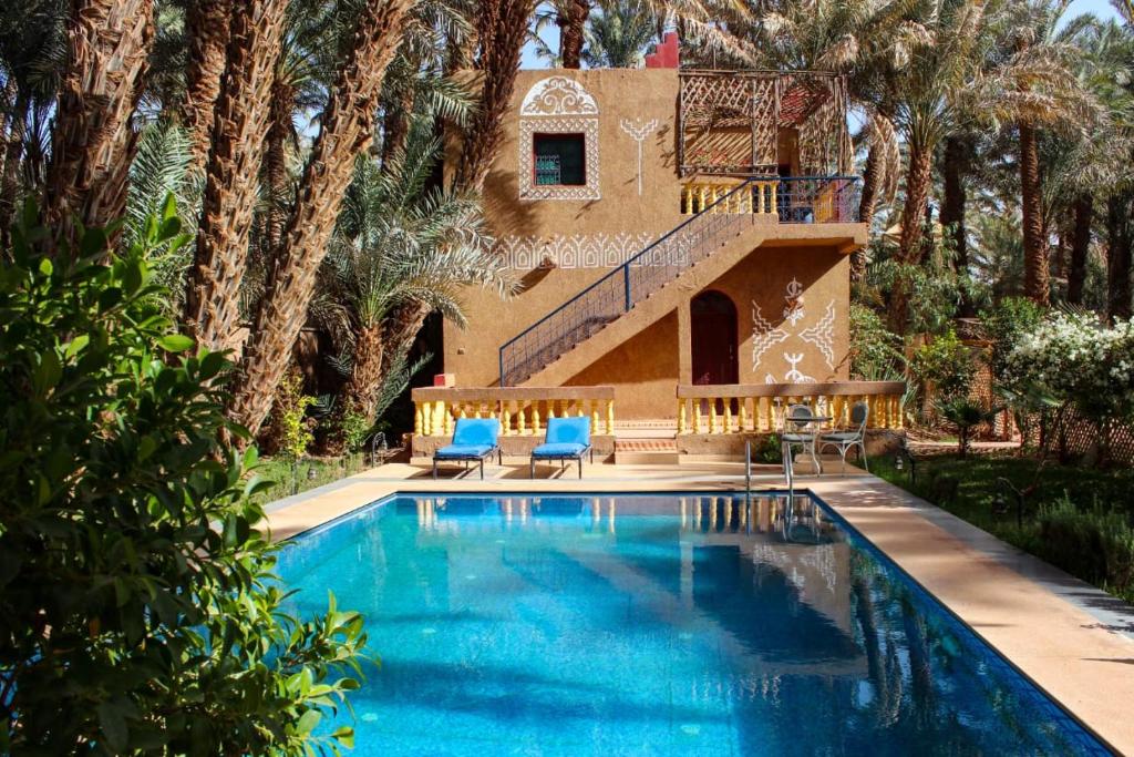 a swimming pool in front of a house with palm trees at Riad auburge soleil in Ksebt nʼAït Hakka