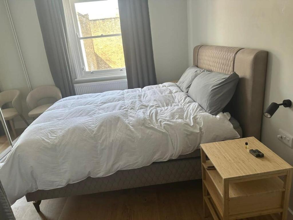 a bed with a white comforter and a table at Abbey Road Luxury Modern Flat w Historic Vibes in London
