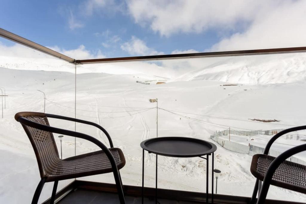 Cozy Studio Ski In Out Apartment In New Gudauri في غودواري: غرفة بها كرسيين وطاولة وجبل مغطى بالثلج