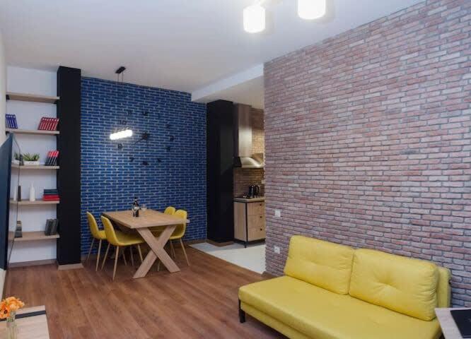 uma sala de estar com um sofá amarelo e uma parede de tijolos em Comfy 3 Apartment house for 9 people em Tbilisi
