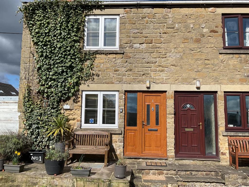 een stenen huis met twee deuren en een bank bij Captivating 2-Bed Cottage in Grewelthorpe in Grewelthorpe