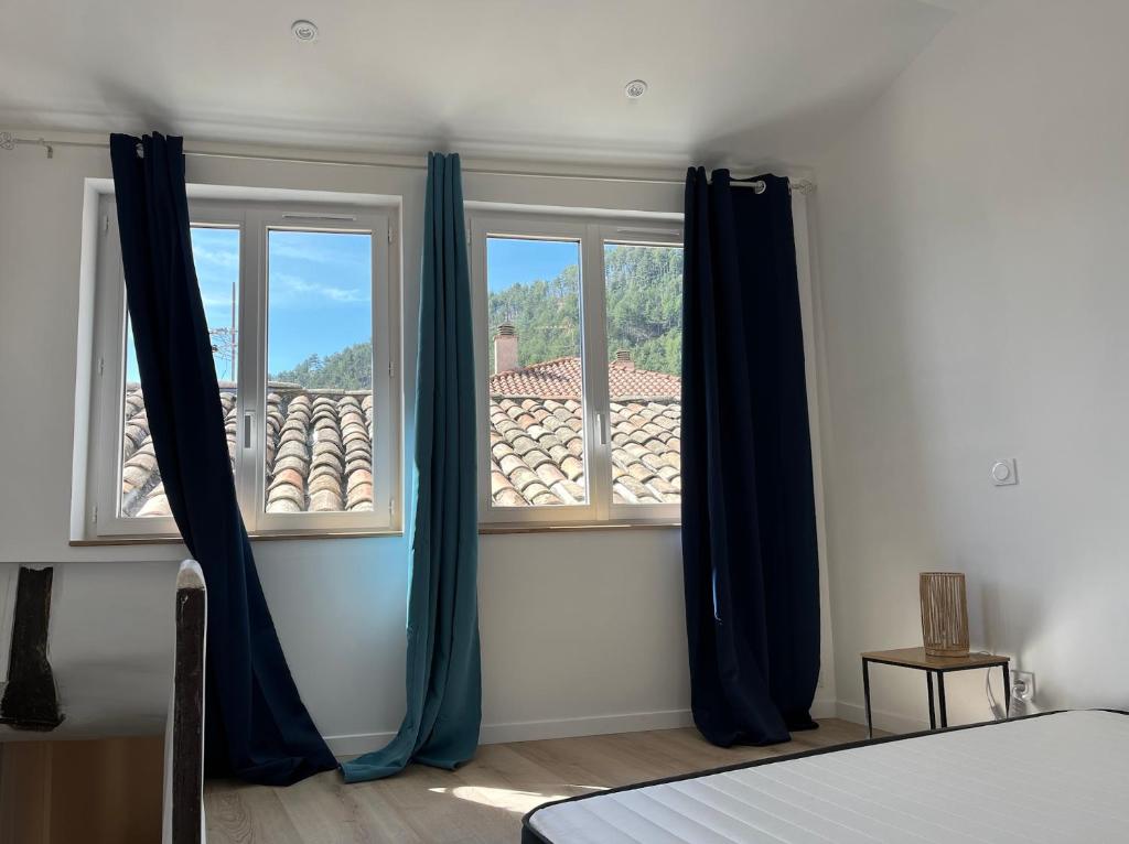 1 dormitorio con 2 ventanas con cortinas azules en Le Jalet en Provence - Penthouse, en Sisteron