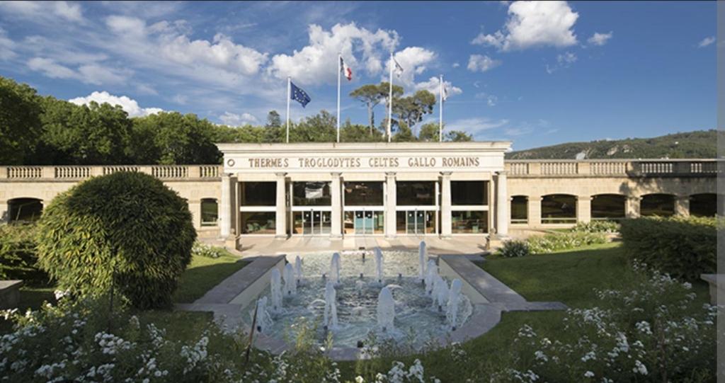 un bâtiment avec une fontaine devant un bâtiment dans l'établissement Appartement climatisé Parc Paradis 150 m des thermes, à Gréoux-les-Bains