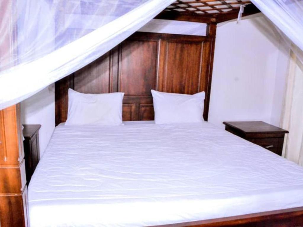 キガリにあるKEZA Homeの白いベッド1台(木製ヘッドボード付)が備わるベッドルーム1室が備わります。
