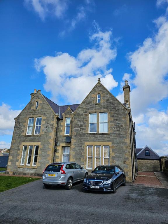 deux voitures garées devant un grand bâtiment en briques dans l'établissement Craigielea Apartment 3, à Lerwick