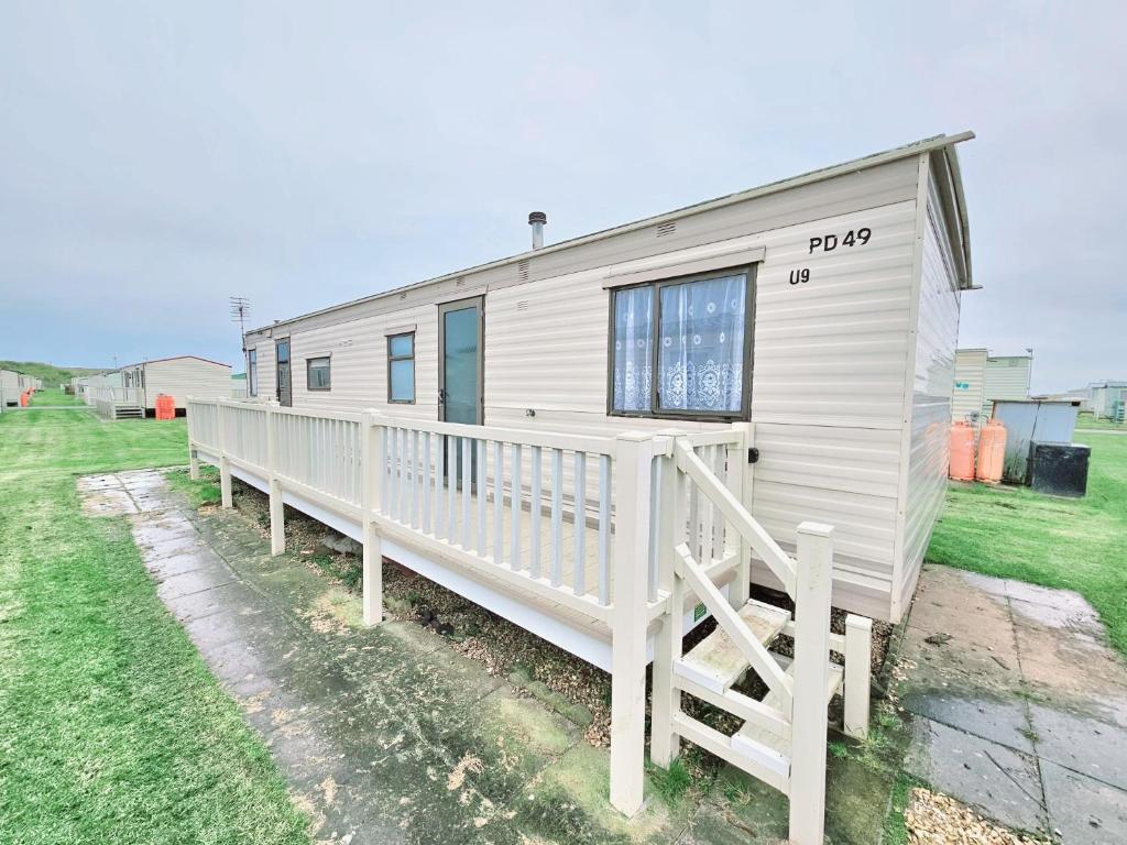 a white mobile home with a porch and a fence at Golden Anchor 8b9 Caravan Park Holiday Home in Chapel Saint Leonards