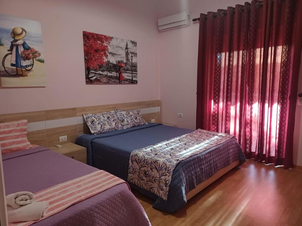 een slaapkamer met 2 bedden en een raam met rode gordijnen bij Apartment Eclipse in Sarandë