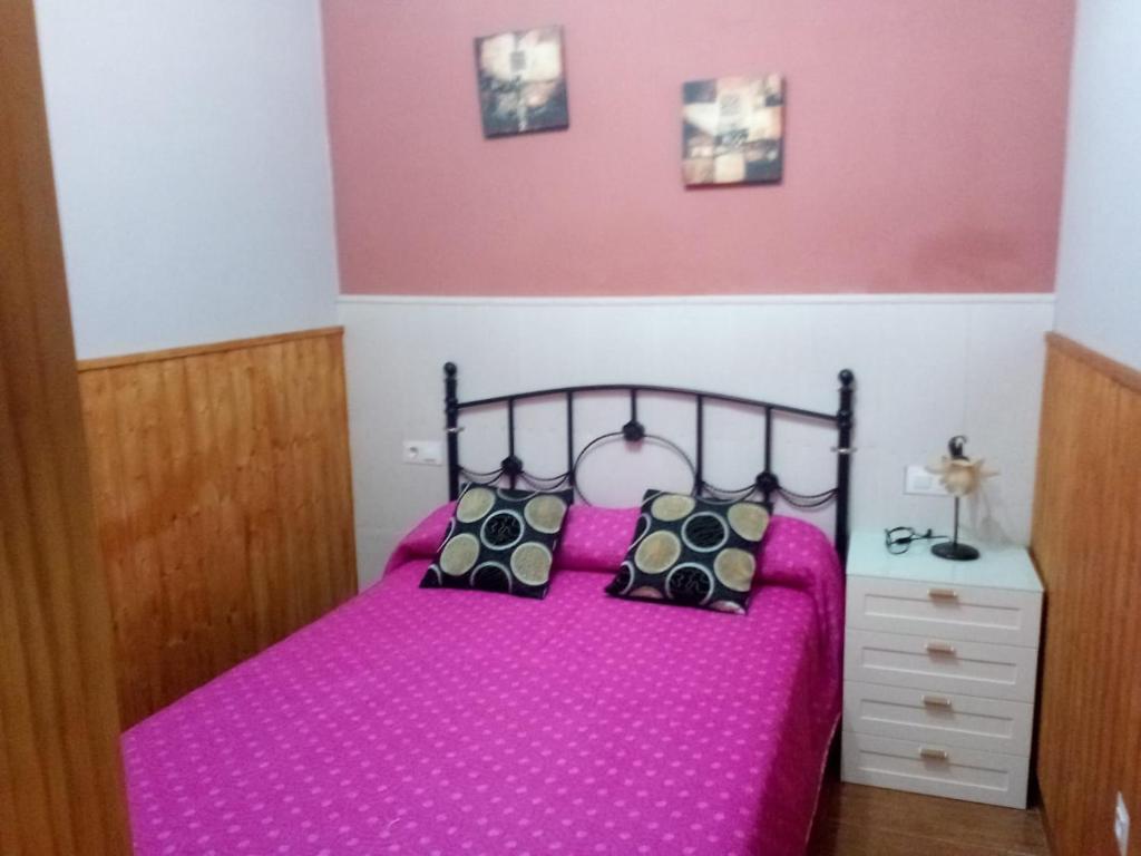 1 dormitorio con cama rosa y almohadas negras en Apartamento araceli en Chipiona
