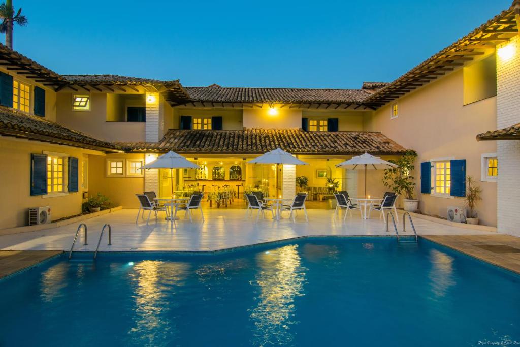 a pool in front of a house with chairs and umbrellas at Hotel Doce Mar in Búzios