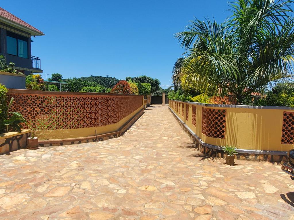 a brick walkway with a fence and palm trees at Alice Gardens and Campsite in Entebbe
