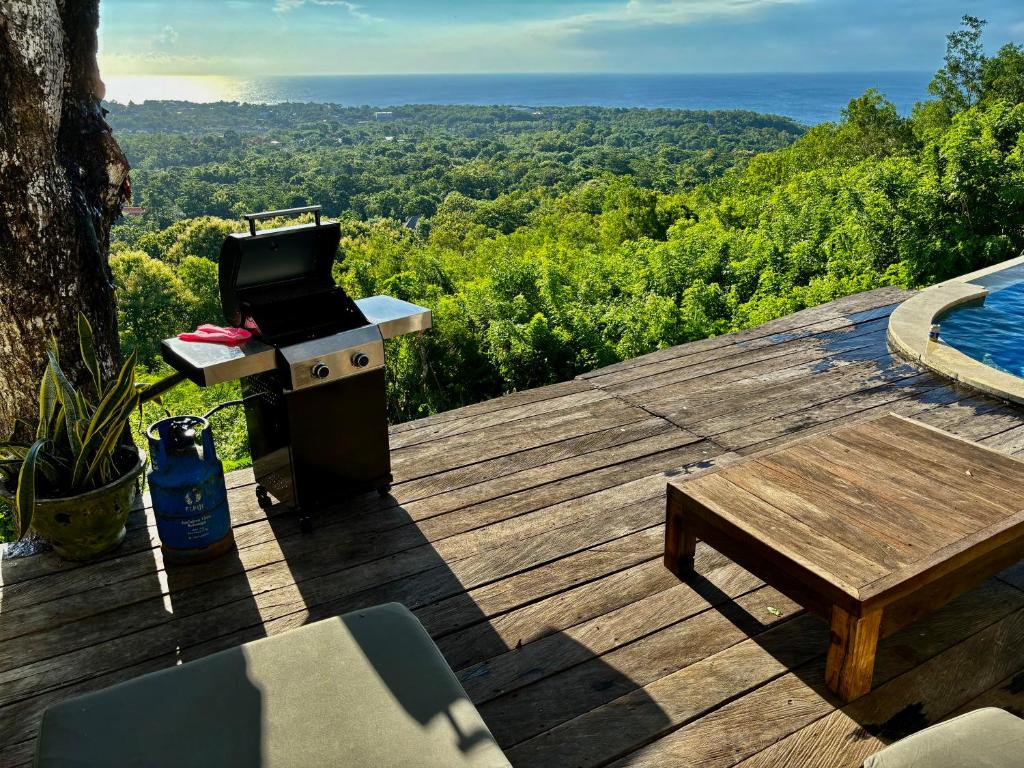a barbecue on a wooden deck with a table and a pool at Padawatu Villas in Uluwatu