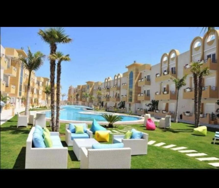 a resort yard with couches and a pool with palm trees at Résidence dunes du golf kantaoui in Sousse