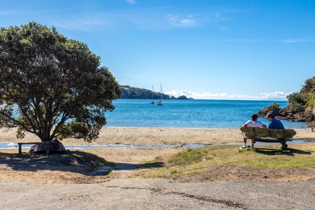 two people sitting on a bench at the beach at Little Ocean Hideaway in Oneroa