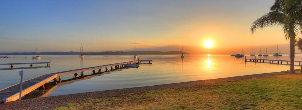 a sunset over a body of water with boats at Paradise Palms Caravan Park in Rathmines