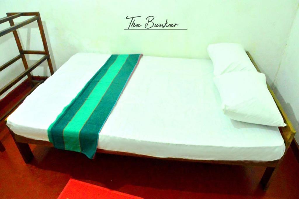 a white bed with a green and white blanket on it at The Bunker in Badulla