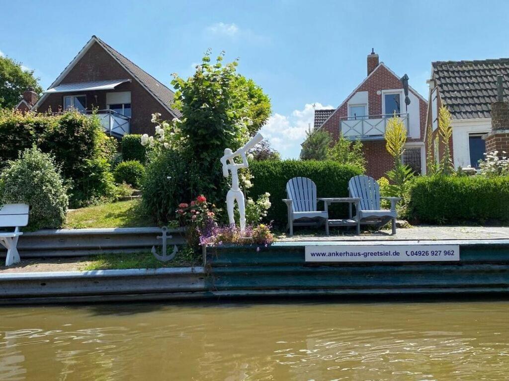 - un jardin avec deux chaises et une statue à côté d'une rivière dans l'établissement Beautiful view in the anchor house on the Siel, à Greetsiel