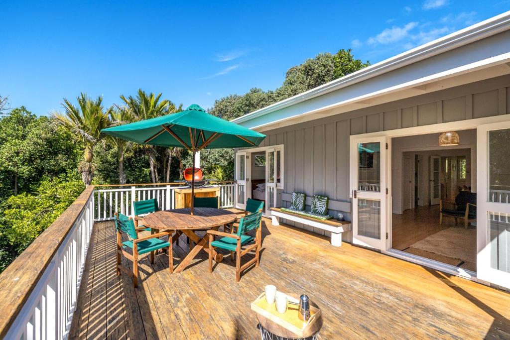 una terraza con mesa, sillas y sombrilla en Nikau Cottage - Palm Beach Holiday Home, en Palm Beach