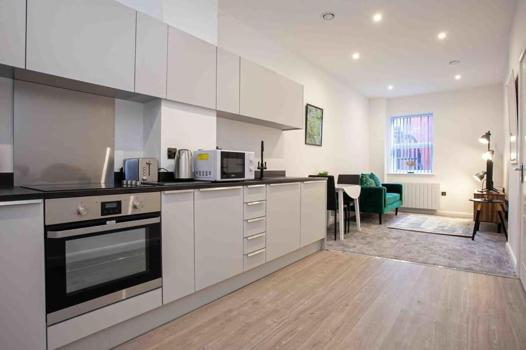a kitchen with white cabinets and a living room at Modern & Stylish 1 Bedroom Apartment in Bolton in Bolton
