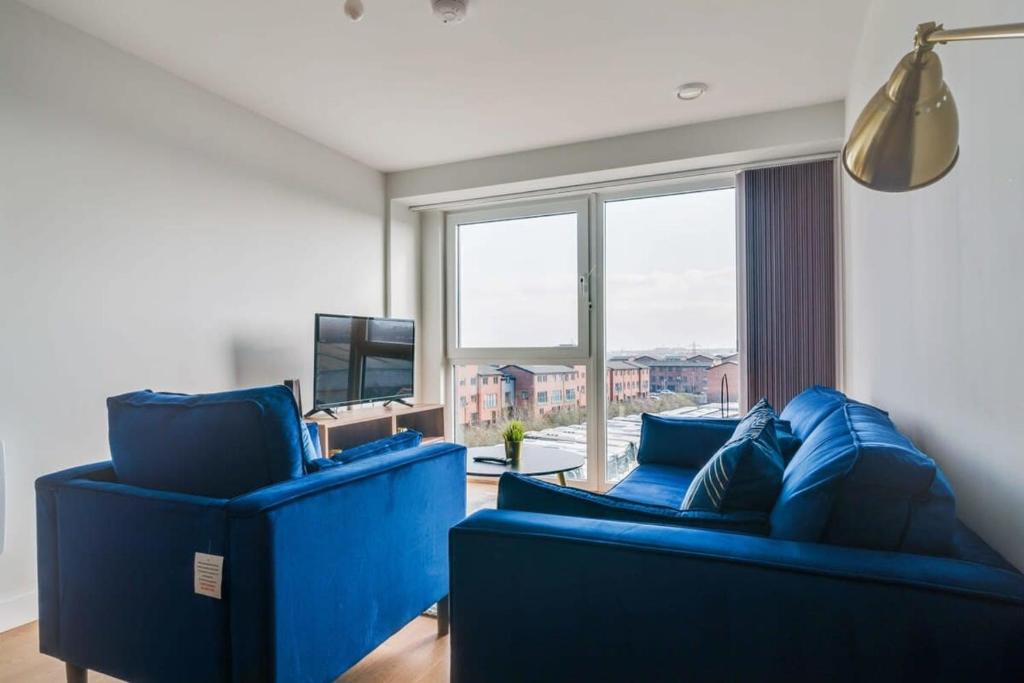 una sala de estar con muebles azules y una gran ventana. en Lovely Riverside 2 Bed Apartment, en Leeds