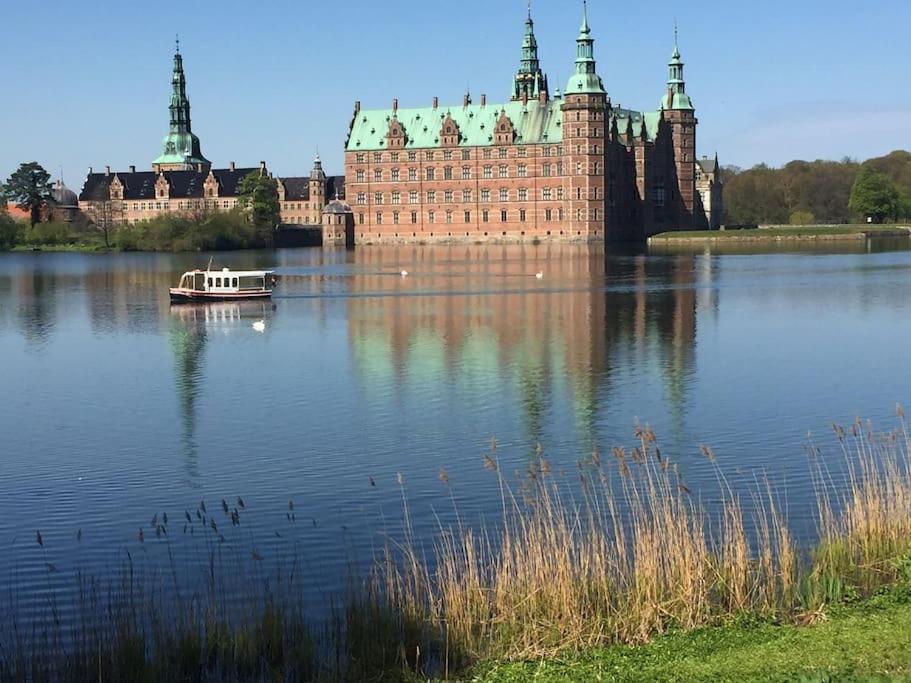 a boat in the water in front of a castle at Cozy, quiet guest house perfect for business or pleasure in Hillerød