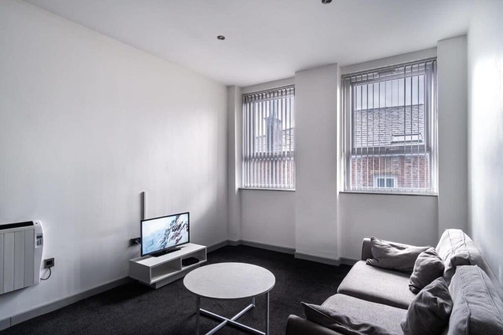 een woonkamer met een bank, een tv en 2 ramen bij Lovely 1 Bed Apartment in Central Blackburn in Blackburn