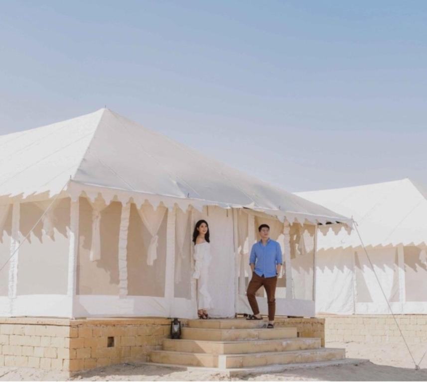 Un uomo e una donna in piedi dentro una tenda bianca di Sam Safari Resort Jaisalmer a Jaisalmer