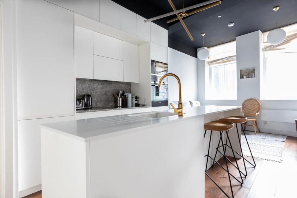 a white kitchen with a large counter and stools at Stunning 1 Bedroom Apartment in Holborn London in London