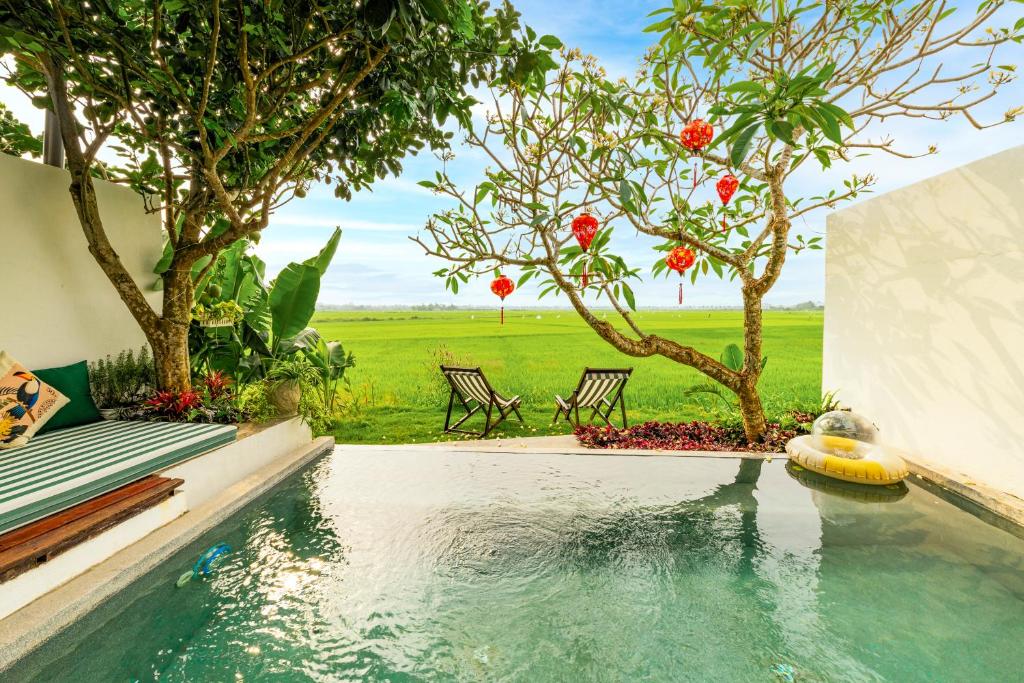 a swimming pool with a tree and some chairs at Min's House Hoi An - 4 bedroom villa, pool in Hoi An