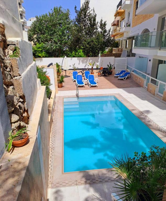a swimming pool with blue chairs and a building at 2Bed flat w shared heated pool in MLH by Homely! in Mellieħa